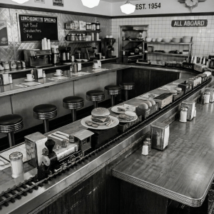 Waitress placing food on a diner counter served by a miniature train carrying plates
